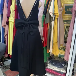 Black Midi Dress in V-neckline on both the front and back, with a prominent oversized bow detail at the waist.