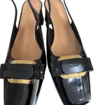 Black patent leather slingback pumps in a square toe and a bold metal buckle on the instep.