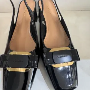 Black patent leather slingback pumps in a square toe and a bold metal buckle on the instep.