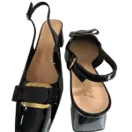 Black patent leather slingback pumps in a square toe and a bold metal buckle on the instep.