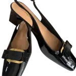 Black patent leather slingback pumps in a square toe and a bold metal buckle on the instep.